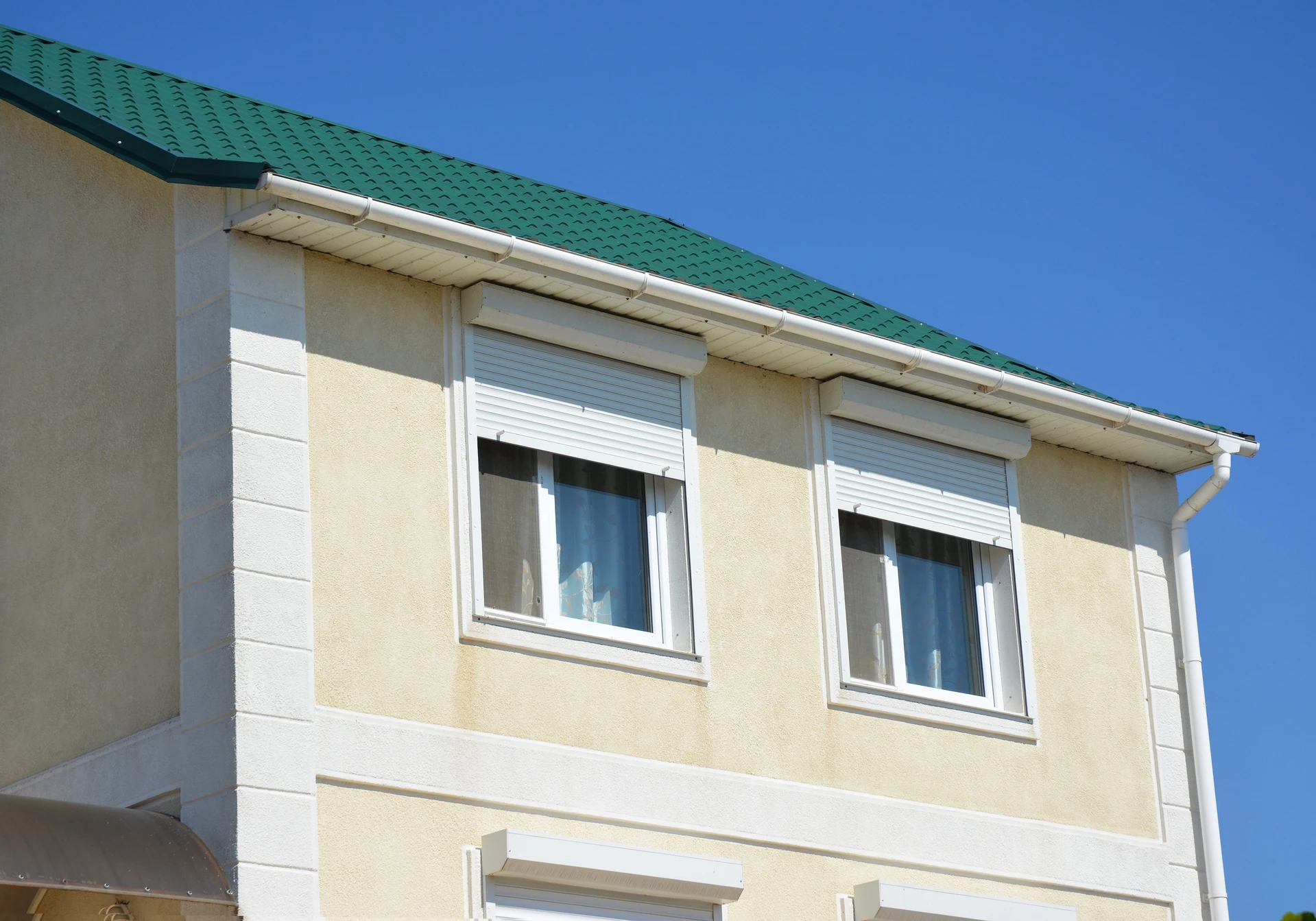 Façade de maison résidentielle avec deux fenêtres à volets roulants blancs partiellement ouverts