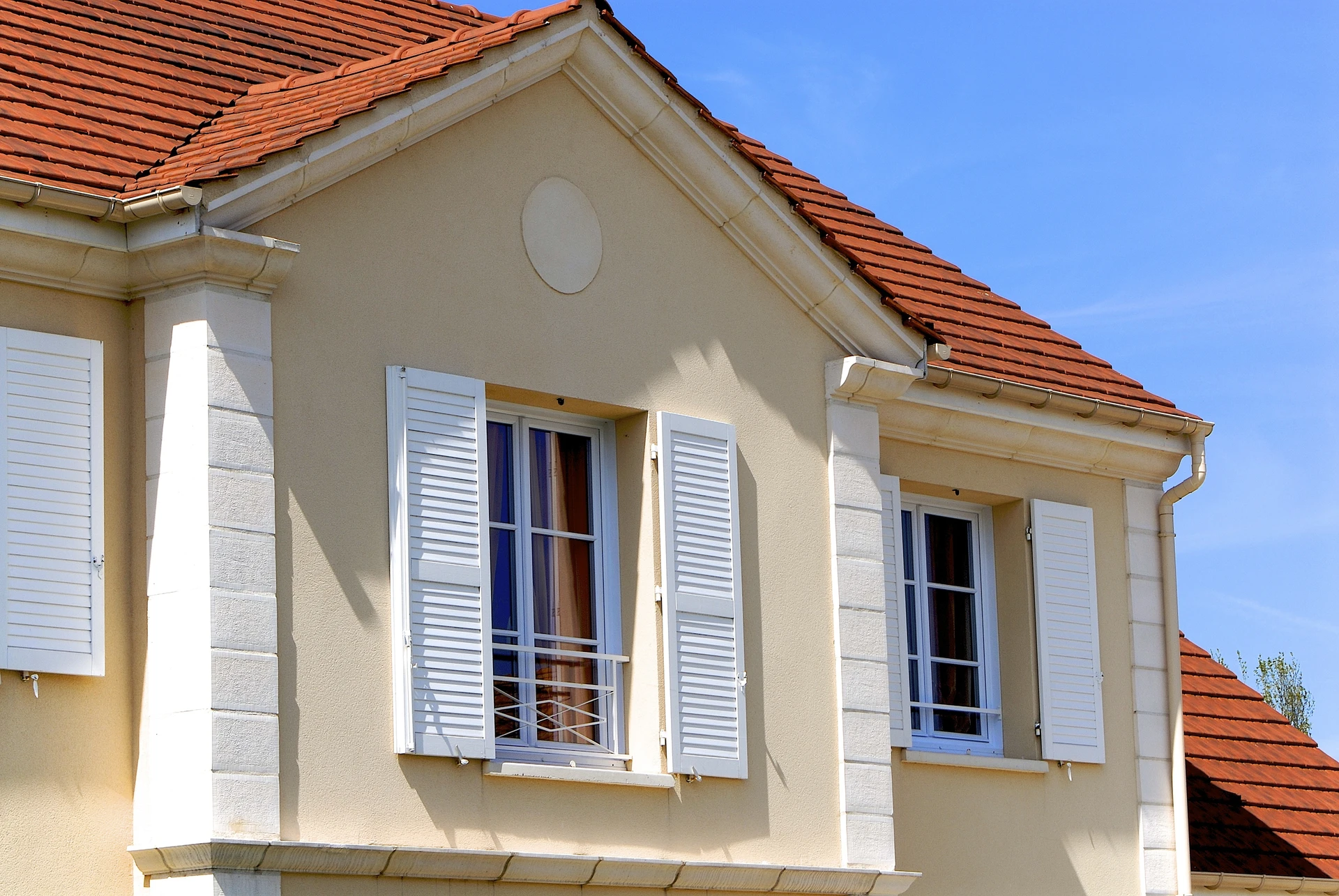 Façade de maison résidentielle avec volets blancs ouverts, fenêtres à petits carreaux et garde-corps métalliques