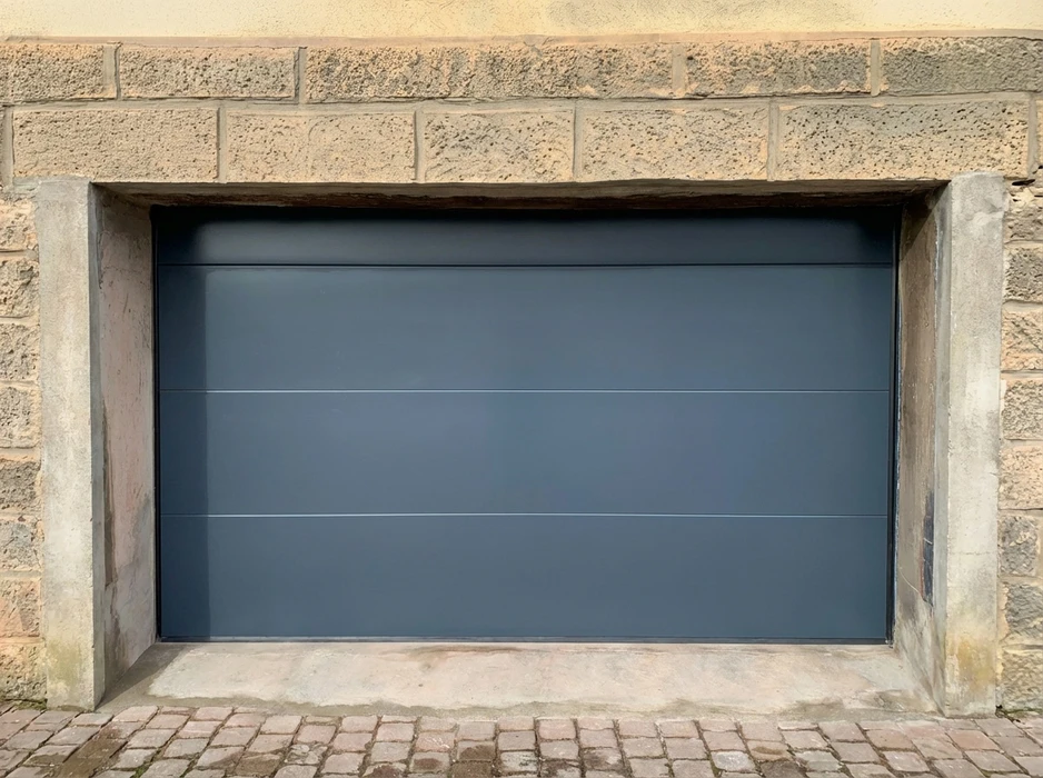 Porte de garage sectionnelle, finition lisse, coloris gris anthracite RAL 7016, montée en applique dans une baie maçonnée en pierre de taille calcaire