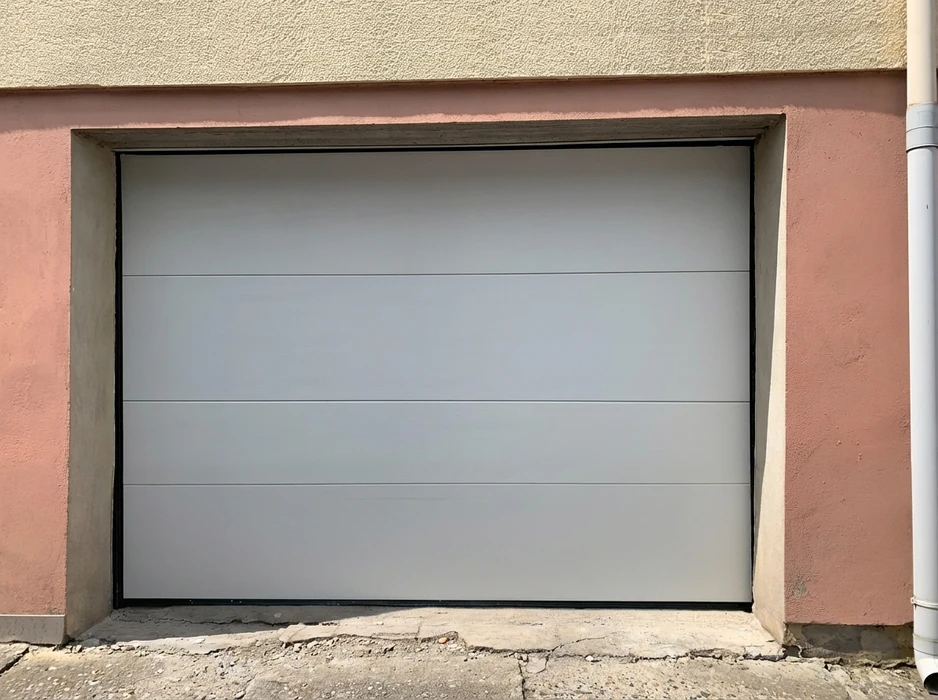 Porte de garage sectionnelle installée en façade extérieure d'un bâtiment à enduit rose