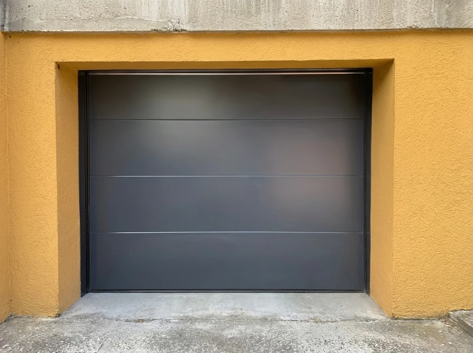 Porte de garage sectionnelle lisse, coloris gris anthracite RAL 7016, montée en applique dans une baie maçonnée enduite jaune ocre