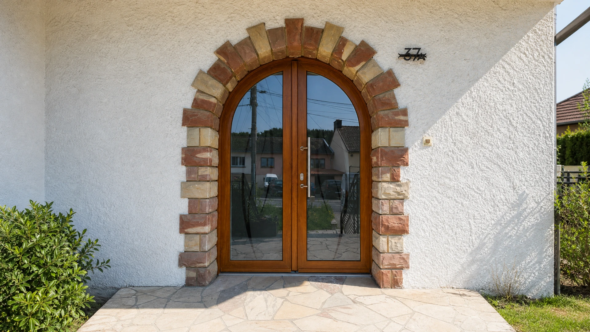 Entrée moderne d'une maison contemporaine avec porte d'entrée noire à poignée verticale intégrée et baies vitrées adjacentes